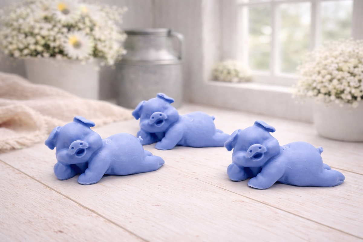 Three cute laughing pig-shaped vegan soap gift set on a wooden surface with flowers in the background