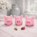 A set of three handmade vegan soaps sculpted into cute pigs with round snouts and floppy ears, displayed with a small decorative bee and ladybird on a white wooden surface.