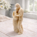 A 3D handmade vegan soap in a warm cream tone, sculpted into a standing figure of a pregnant couple; the partner stands behind the expectant mother, tenderly cradling her baby bump, displayed on a light wooden surface in a bright farmhouse setting.