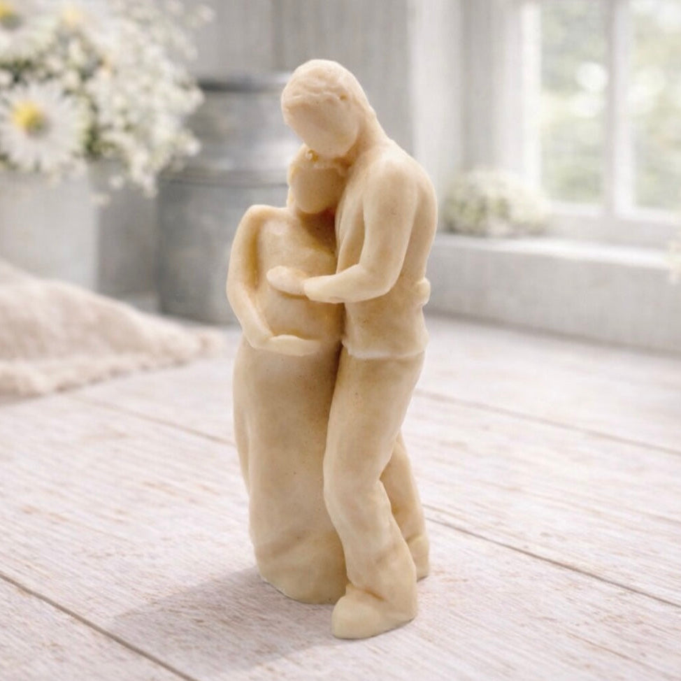 A 3D handmade vegan soap in a warm cream tone, sculpted into a standing figure of a pregnant couple; the partner stands behind the expectant mother, tenderly cradling her baby bump, displayed on a light wooden surface in a bright farmhouse setting.