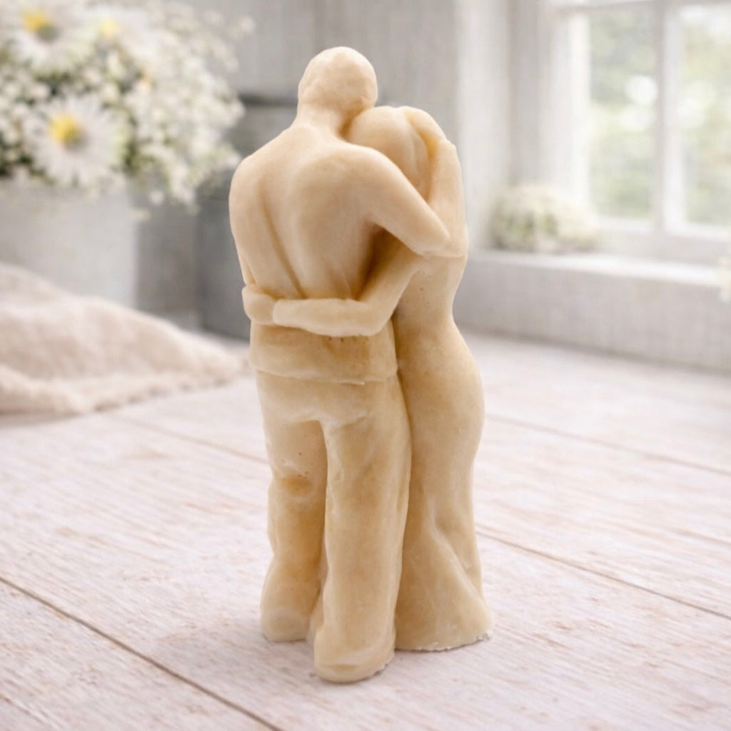 A 3D handmade vegan soap in a warm cream tone, sculpted into a standing figure of a pregnant couple; the partner stands behind the expectant mother, tenderly cradling her baby bump, displayed on a light wooden surface in a bright farmhouse setting.