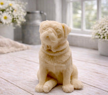 Load image into Gallery viewer, A detailed handmade vegan soap sculpted in the shape of a sitting pug dog with characteristic facial wrinkles and a tilted head, in a charcoal-grey tone, displayed on a light wooden surface.
