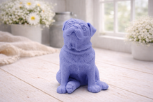 Load image into Gallery viewer, A detailed handmade vegan soap sculpted in the shape of a sitting pug dog with characteristic facial wrinkles and a tilted head, in a charcoal-grey tone, displayed on a light wooden surface.
