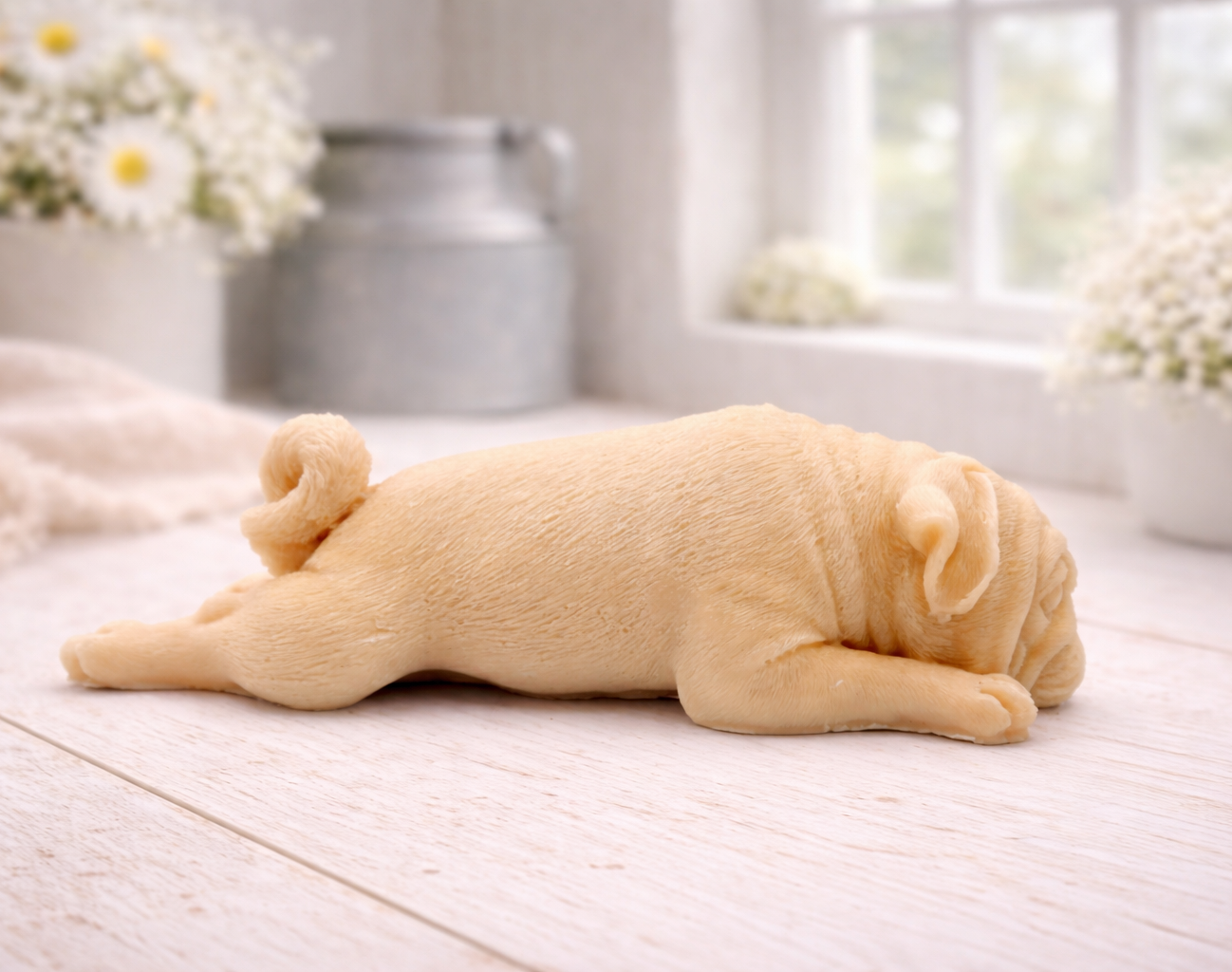 A detailed handmade vegan soap gift, sculpted in the shape of a pug dog lying flat on its stomach in a sleeping position, showing realistic skin folds and fur texture, displayed on a light wooden surface. Handmade in Blackpool 