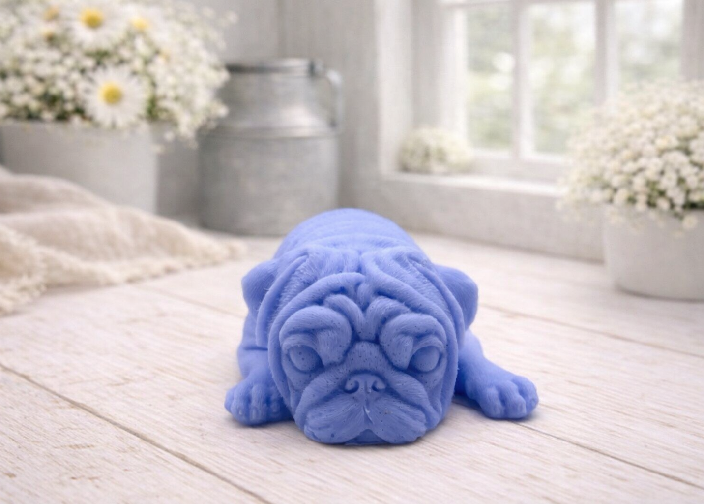 A detailed handmade vegan soap gift, sculpted in the shape of a pug dog lying flat on its stomach in a sleeping position, showing realistic skin folds and fur texture, displayed on a light wooden surface. Handmade in Blackpool 