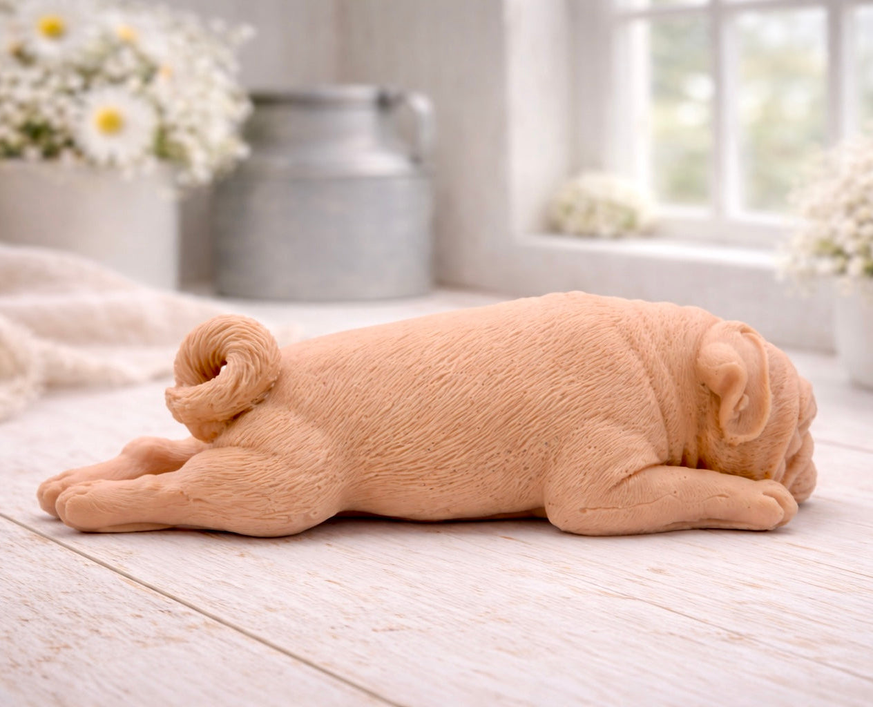 A detailed handmade vegan soap gift, sculpted in the shape of a pug dog lying flat on its stomach in a sleeping position, showing realistic skin folds and fur texture, displayed on a light wooden surface. Handmade in Blackpool 