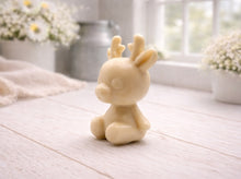 Load image into Gallery viewer, A 3D handmade vegan soap crafted into a cute, sitting baby reindeer with small antlers, rounded features, and a sweet expression, set against a bright farmhouse window.
