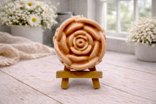 Load image into Gallery viewer, A handmade vegan soap, intricately sculpted in the shape of a large, blooming rose flower with layered petals, displayed on a small wooden easel against a bright win
