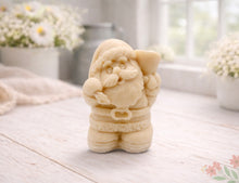 Load image into Gallery viewer, A highly detailed 3D handmade vegan soap featuring a Father Christmas carrying a large sack of gifts over his shoulder and holding a bell, featuring an intricate curly beard and fur-trimmed suit, set against a festive holiday background.

