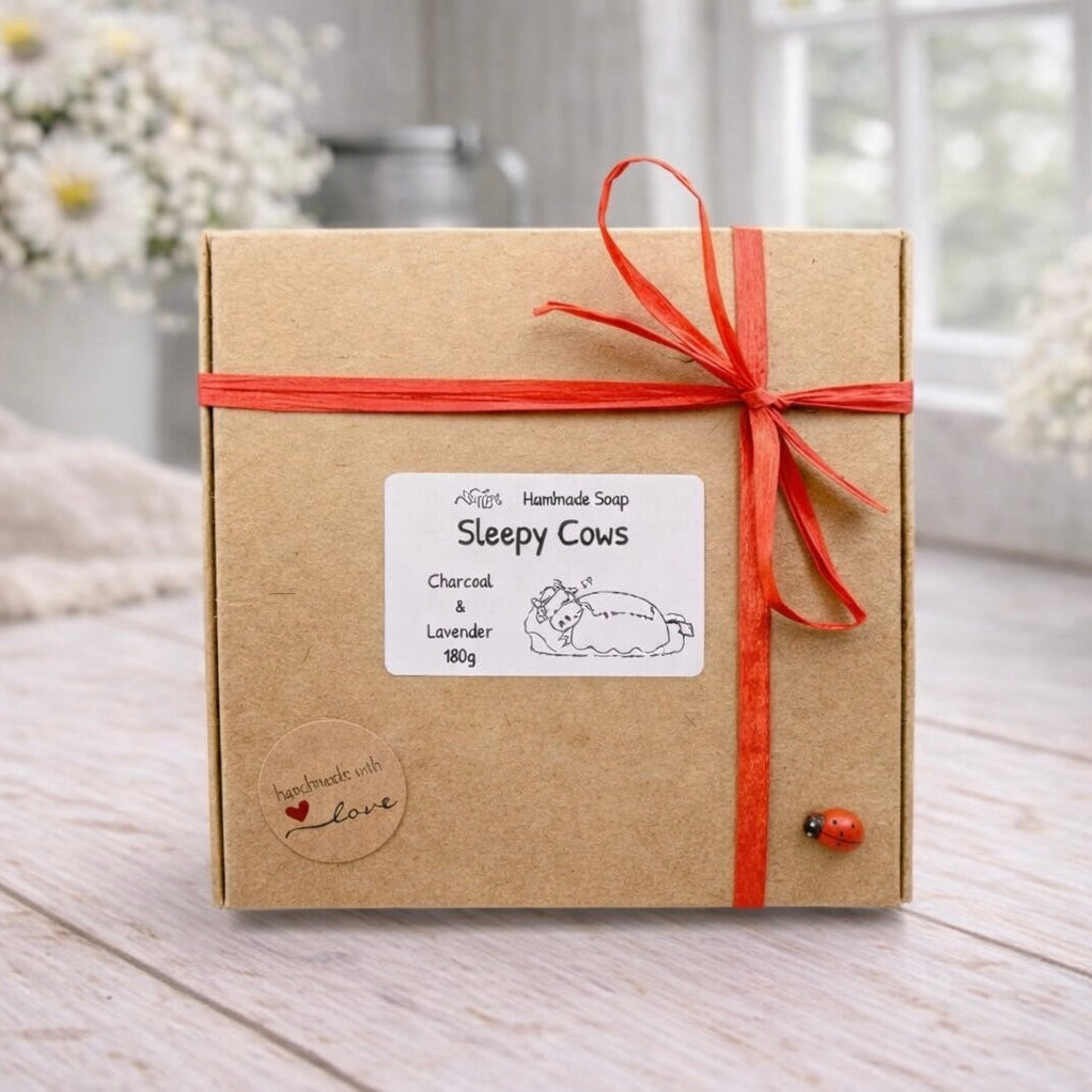 Box of 'Sleepy Cows' handmade soap with a red ribbon on a wooden surface.