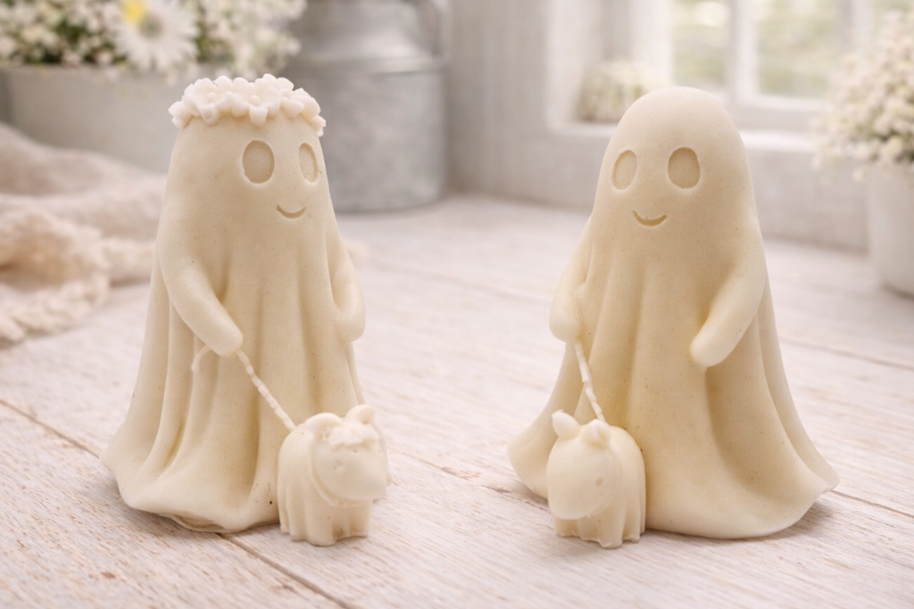Two white ghost vegan soaps with small dogs on a wooden surface with flowers in the background