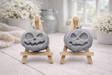 Load image into Gallery viewer, A collection of six handmade vegan Halloween soaps in a mottled grey and black charcoal finish, featuring a smiling bat, three different carved pumpkins (one wearing a witch's hat), a ghost, and a skull, arranged on and around a small wooden easel.
