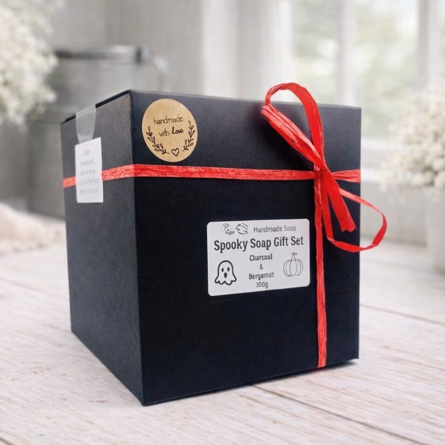 Black gift box with red ribbon and 'Spooky Soap Gift Set' label on a light wooden surface.