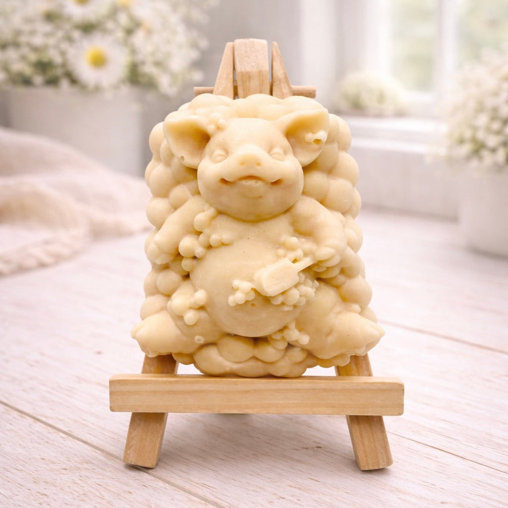 A detailed handmade vegan soap, sculpted as a cheerful pig sitting in a mound of bubbles and holding a scrubbing brush, displayed on a miniature wooden easel against a soft farmhouse window background 