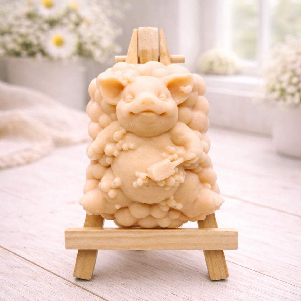 A detailed handmade vegan soap, sculpted as a cheerful pig sitting in a mound of bubbles and holding a scrubbing brush, displayed on a miniature wooden easel against a soft farmhouse window background 