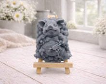 Load image into Gallery viewer, A detailed handmade vegan soap, sculpted as a cheerful pig sitting in a mound of bubbles and holding a scrubbing brush, displayed on a miniature wooden easel against a soft farmhouse window background 
