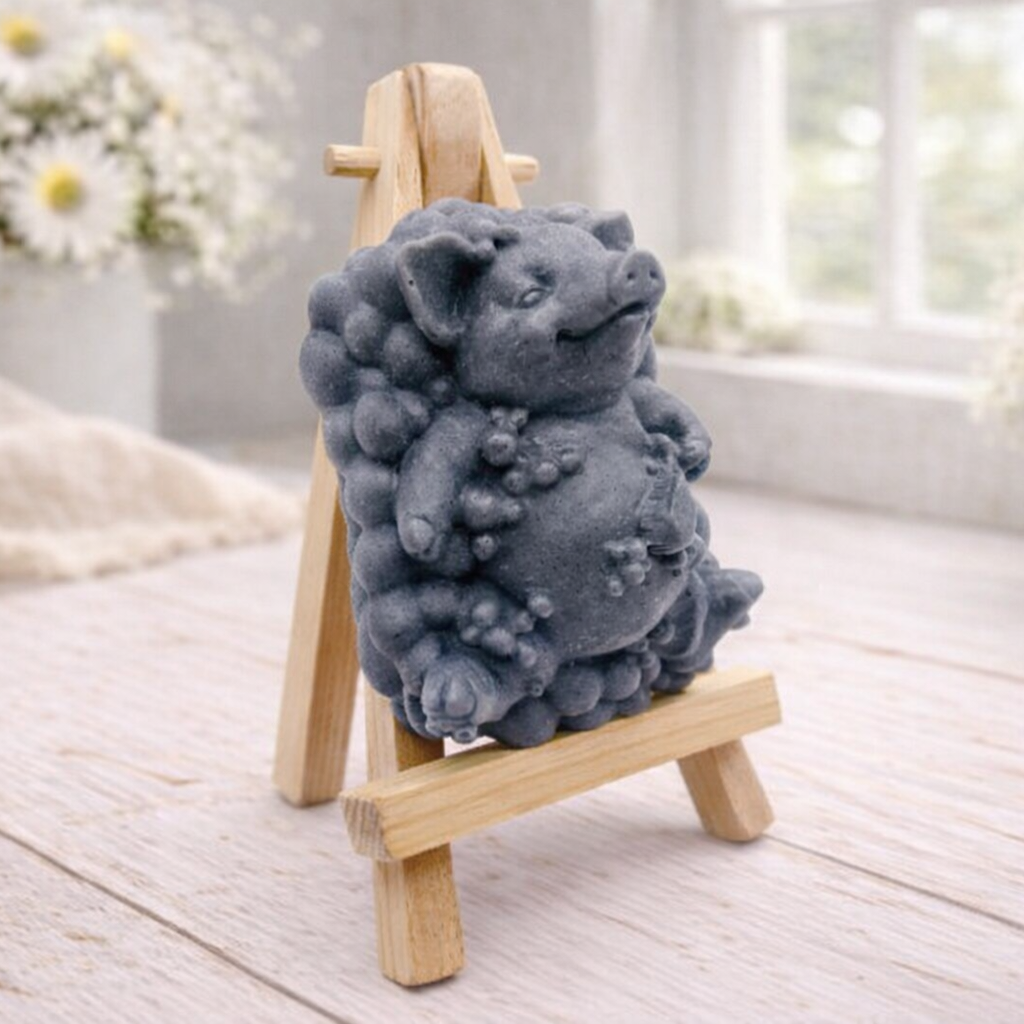 A detailed handmade vegan soap, sculpted as a cheerful pig sitting in a mound of bubbles and holding a scrubbing brush, displayed on a miniature wooden easel against a soft farmhouse window background 