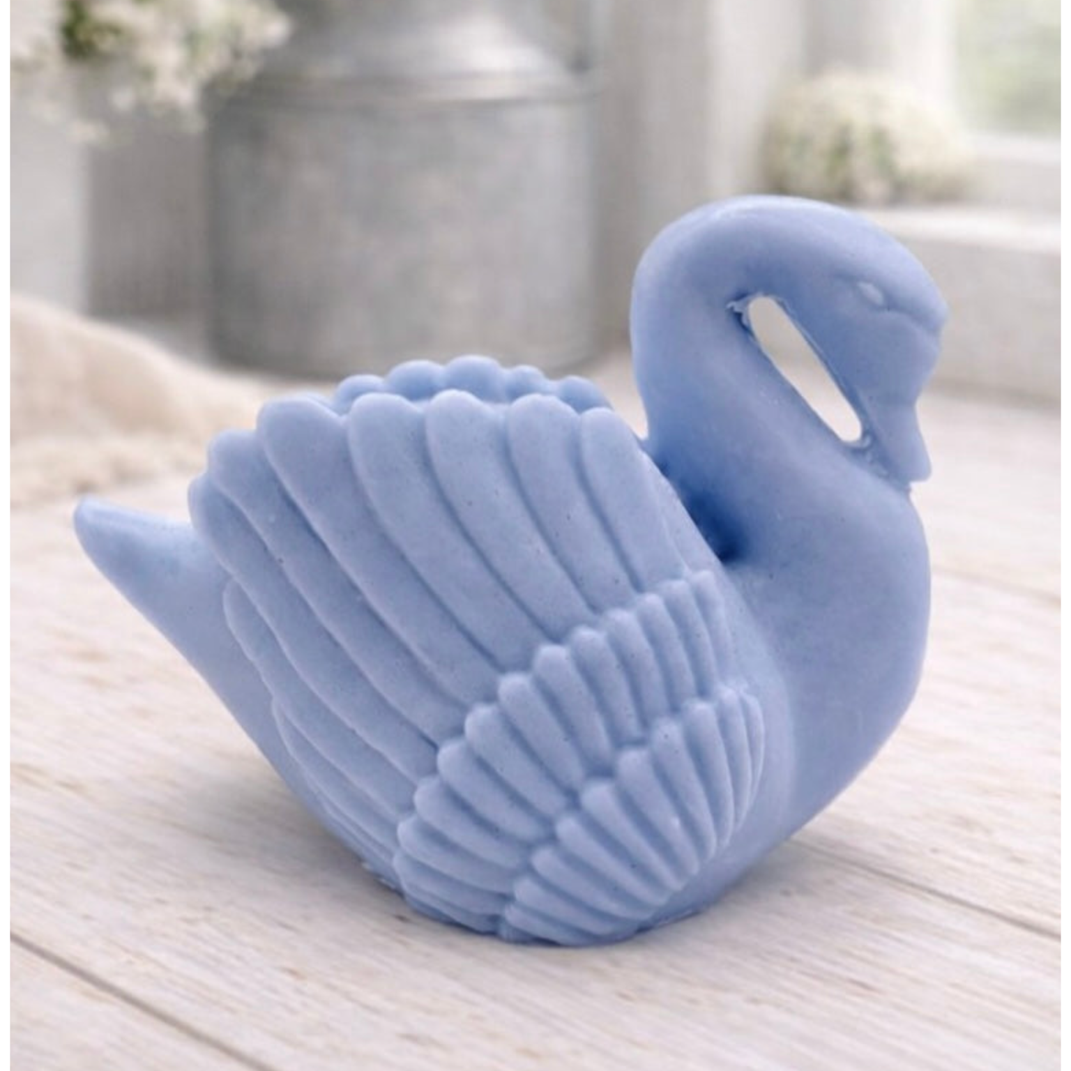 handmade vegan soap, sculpted into the shape of a graceful swan with detailed feathering on its wings and a curved neck, displayed on a light wooden surface in a bright farmhouse setting.