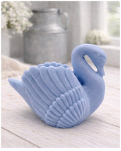 Load image into Gallery viewer, handmade vegan soap, sculpted into the shape of a graceful swan with detailed feathering on its wings and a curved neck, displayed on a light wooden surface in a bright farmhouse setting.
