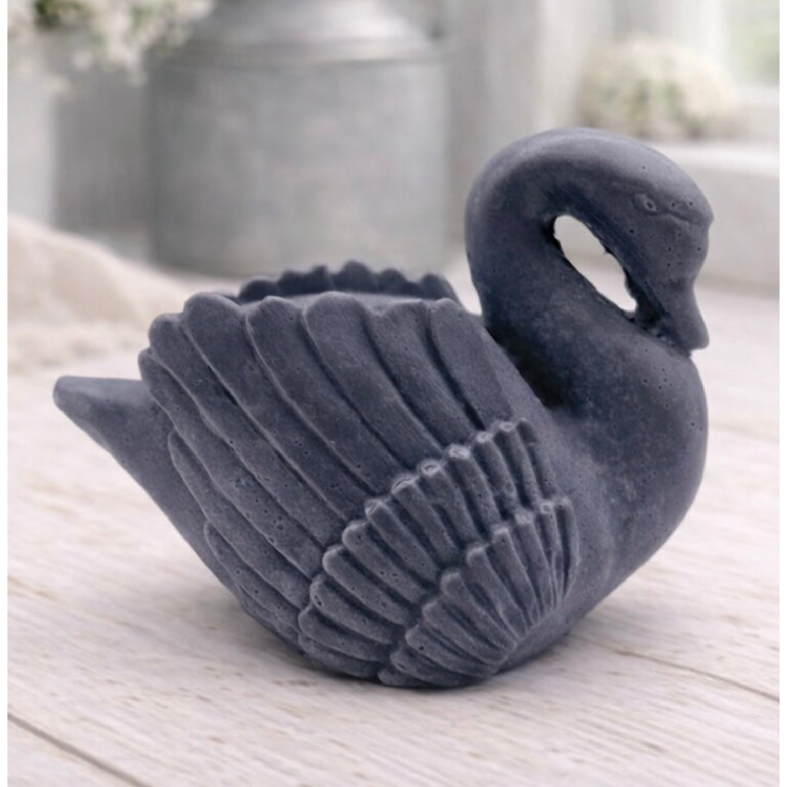 handmade vegan soap, sculpted into the shape of a graceful swan with detailed feathering on its wings and a curved neck, displayed on a light wooden surface in a bright farmhouse setting.