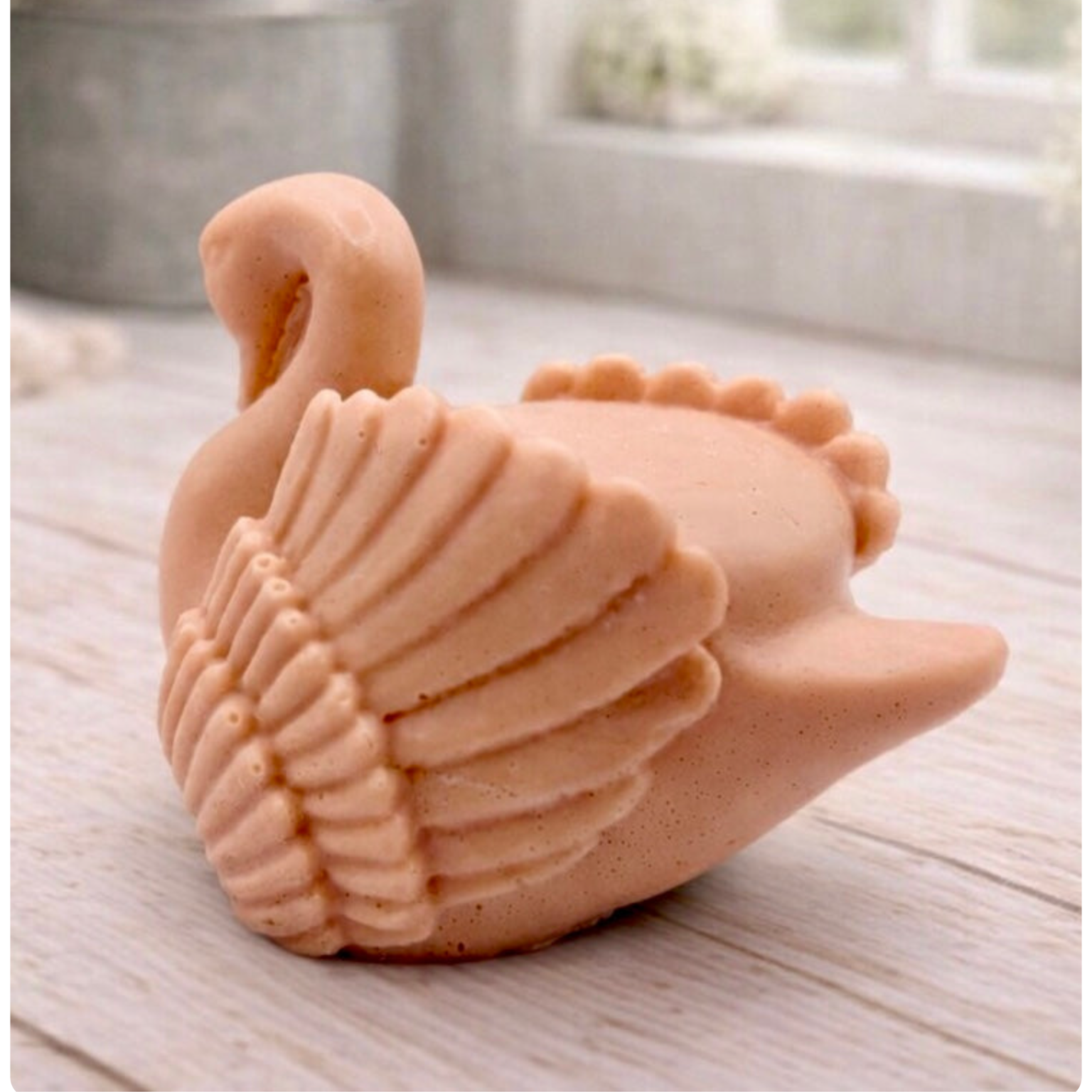 handmade vegan soap, sculpted into the shape of a graceful swan with detailed feathering on its wings and a curved neck, displayed on a light wooden surface in a bright farmhouse setting.