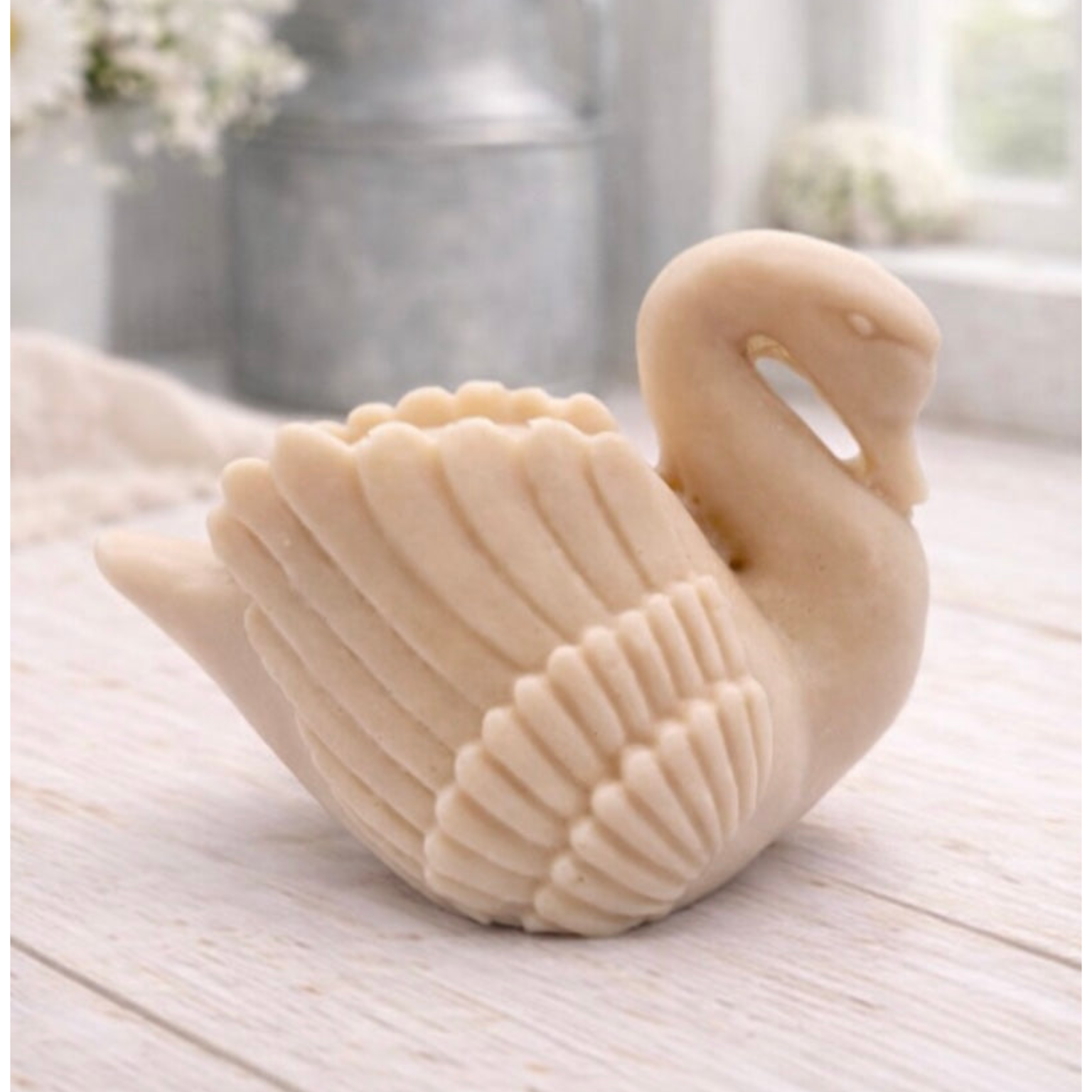 handmade vegan soap, sculpted into the shape of a graceful swan with detailed feathering on its wings and a curved neck, displayed on a light wooden surface in a bright farmhouse setting.