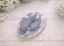 Load image into Gallery viewer, A handmade vegan soap featuring two grey dolphins jumping through white frothy waves; the base is white, and the dolphins are highly detailed, displayed on a light wooden surface against a soft farmhouse background.
