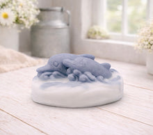 Load image into Gallery viewer, A handmade vegan soap featuring two grey dolphins jumping through white frothy waves; the base is white, and the dolphins are highly detailed, displayed on a light wooden surface against a soft farmhouse background.
