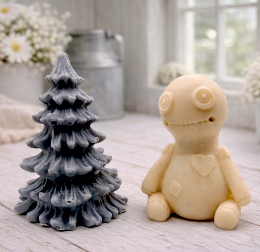 A handmade vegan soap gift set featuring a cream-coloured voodoo doll soap with stitched details and a grey tiered Christmas tree soap, presented in a black gift box tied with a red raffia ribbon and a small ladybird embellishment.