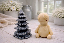 Load image into Gallery viewer, A handmade vegan soap gift set featuring a cream-coloured voodoo doll soap with stitched details and a grey tiered Christmas tree soap, presented in a black gift box tied with a red raffia ribbon and a small ladybird embellishment.
