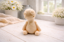 Load image into Gallery viewer, A handmade vegan soap gift in the shape of a stitched voodoo doll with button eyes and a small patch on its chest, sitting on a light wooden surface.
