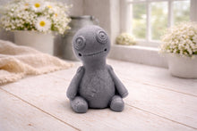 Load image into Gallery viewer, A handmade vegan soap gift in the shape of a stitched voodoo doll with button eyes and a small patch on its chest, sitting on a light wooden surface.
