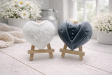 Load image into Gallery viewer, A pair of handmade vegan soaps shaped like hearts and displayed on miniature wooden easels; one heart is textured like a grey tuxedo with a bow tie and buttons, and the other is a white bridal gown heart with intricate lace patterns and a pearl necklace detail.

