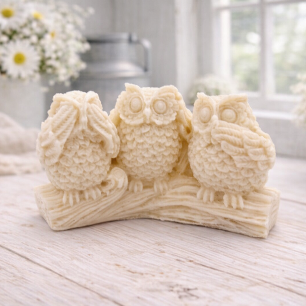 A handmade vegan soap gift featuring three owls perched on a branch in the "See No Evil, Hear No Evil, Speak No Evil" poses, set against a bright window with white flowers.