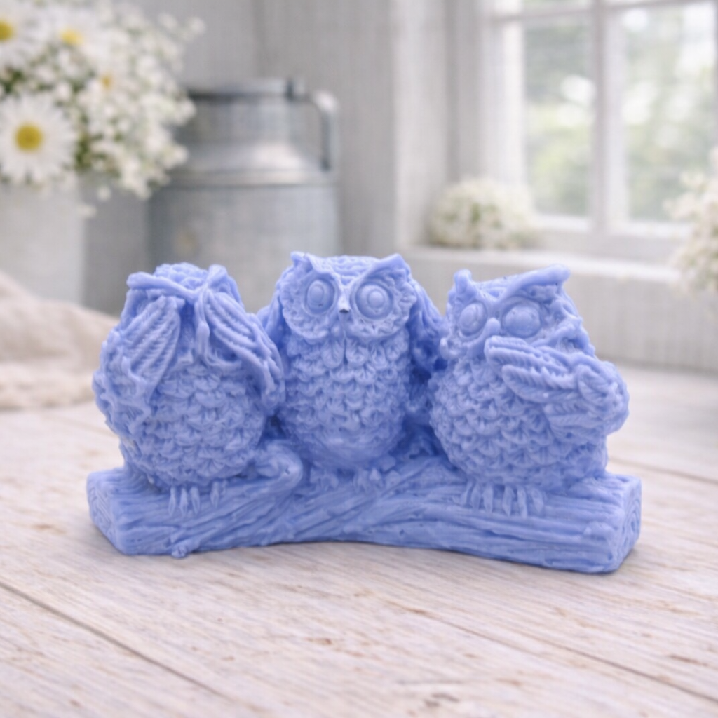A handmade vegan soap gift featuring three owls perched on a branch in the "See No Evil, Hear No Evil, Speak No Evil" poses, set against a bright window with white flowers.