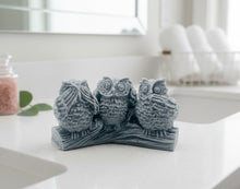 Load image into Gallery viewer, A set of three detailed handmade vegan owl soaps in a "See No, Hear No, Speak No Evil" pose, displayed on a rustic log base with a soft pastel farmhouse decor background.
