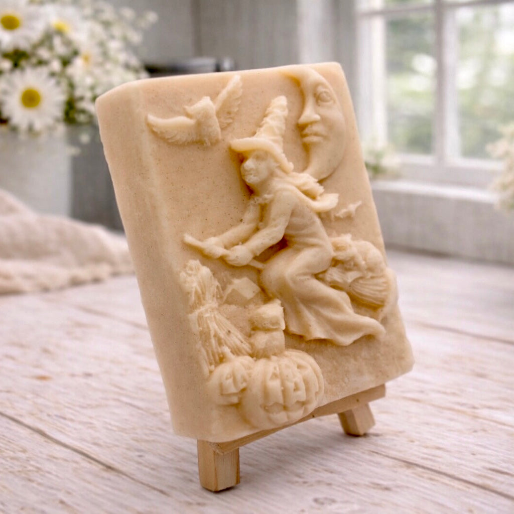 handmade vegan soap bar featuring a detailed relief carving of a witch flying on a broomstick past a crescent moon, owls, and pumpkins.