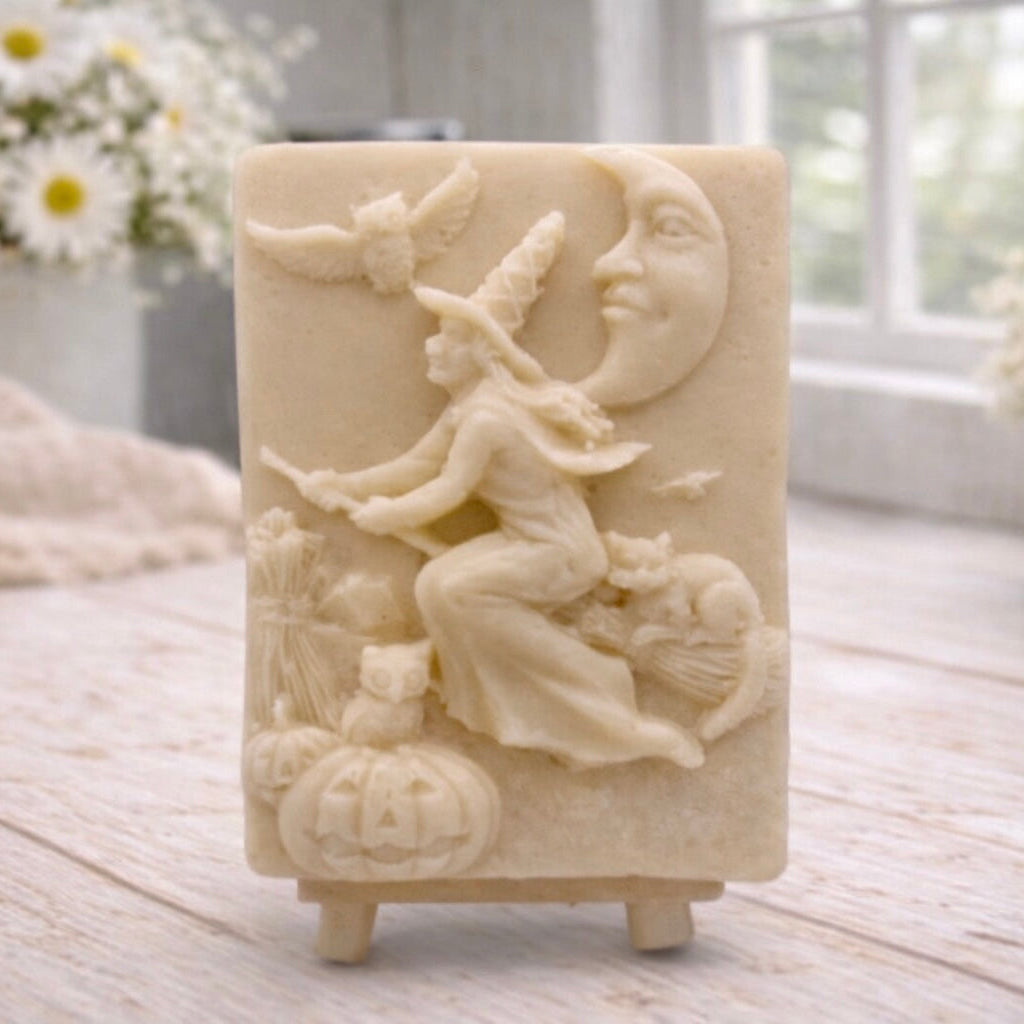 handmade vegan soap bar featuring a detailed relief carving of a witch flying on a broomstick past a crescent moon, owls, and pumpkins.