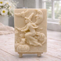handmade vegan soap bar featuring a detailed relief carving of a witch flying on a broomstick past a crescent moon, owls, and pumpkins.
