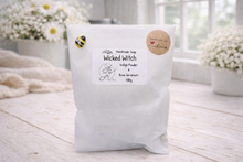 Load image into Gallery viewer, White soap package with a label on a light wooden surface, surrounded by flowers.
