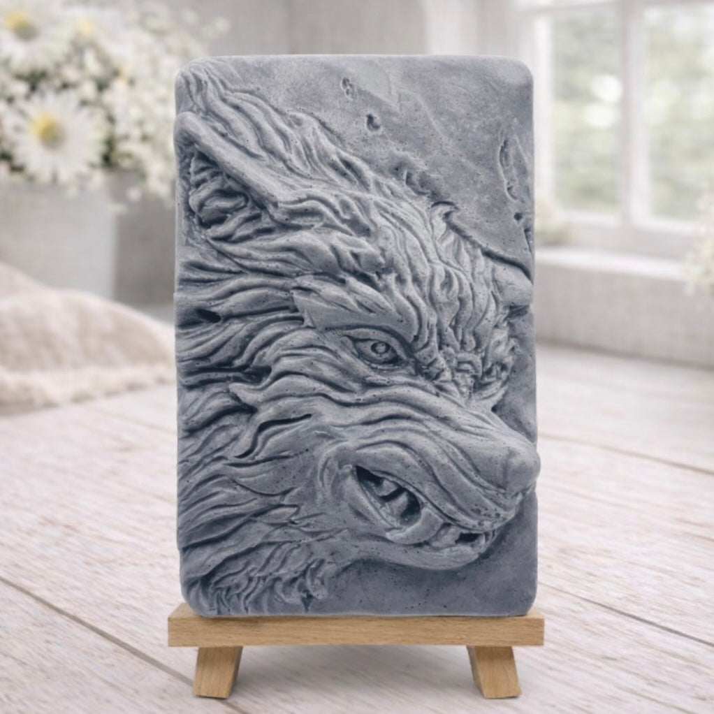 A rectangular handmade vegan soap featuring a highly detailed, 3D relief carving of a wolf's head in profile with a thick, textured mane, displayed on a miniature wooden easel.