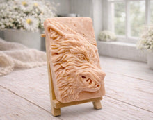 Load image into Gallery viewer, A rectangular handmade vegan soap featuring a highly detailed, 3D relief carving of a wolf's head in profile with a thick, textured mane, displayed on a miniature wooden easel.
