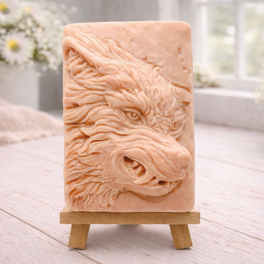 A rectangular handmade vegan soap featuring a highly detailed, 3D relief carving of a wolf's head in profile with a thick, textured mane, displayed on a miniature wooden easel.