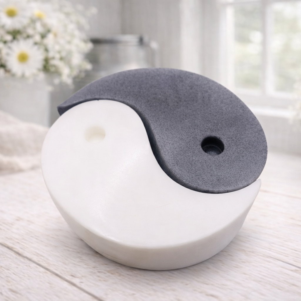A handmade vegan soap gift set featuring two interlocking teardrop-shaped bars in contrasting black and white to form a large yin and yang symbol, displayed on a light wooden surface.