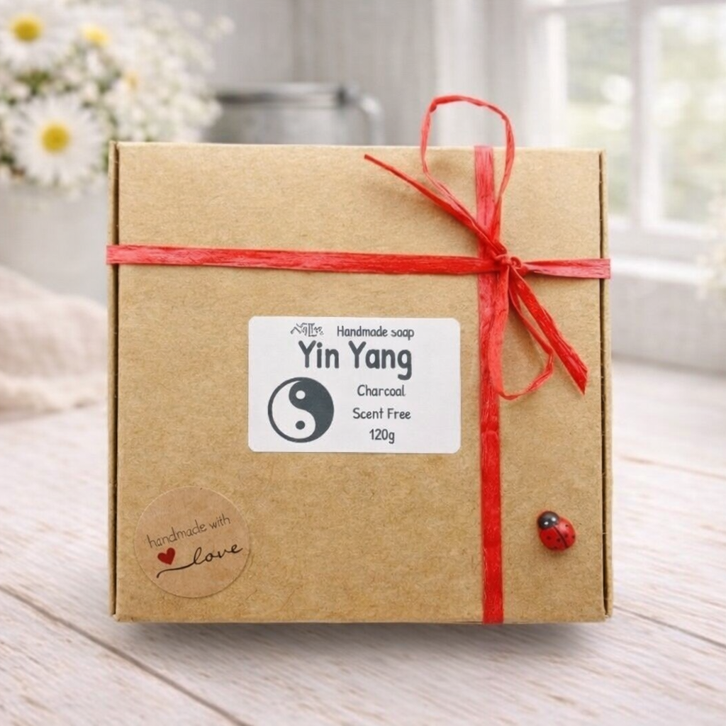 Gift box with a red ribbon and 'Yin Yang' label on a wooden surface with flowers in the background