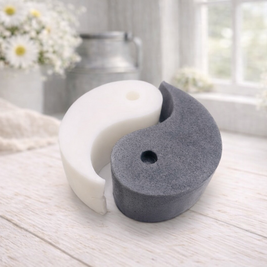 A handmade vegan soap gift set featuring two interlocking teardrop-shaped bars in contrasting black and white to form a large yin and yang symbol, displayed on a light wooden surface.