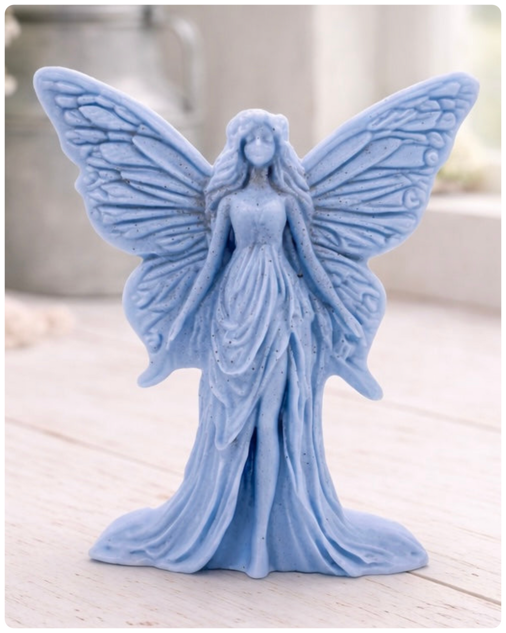 A detailed handmade vegan soap featuring an elegant fairy with large, intricate butterfly-style wings, a flowing gown, and long hair, standing against a bright farmhouse window background.
