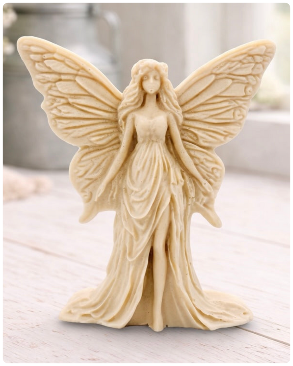 A detailed handmade vegan soap featuring an elegant fairy with large, intricate butterfly-style wings, a flowing gown, and long hair, standing against a bright farmhouse window background.